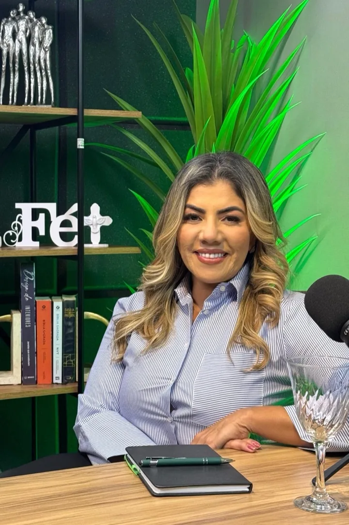 Irineia Barbosa no estúdio do podcast Voz que Eleva, ao lado de uma estante com a palavra Fé